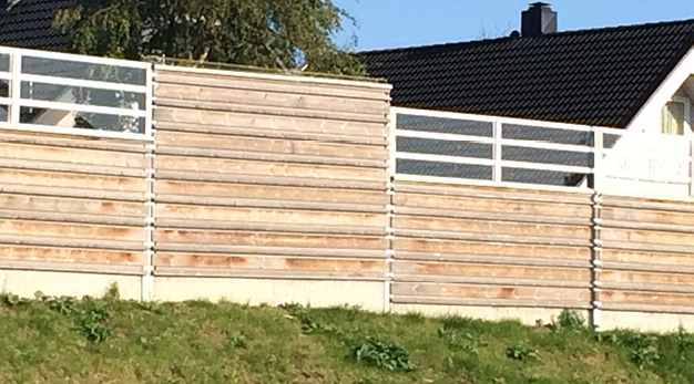 Bullerstaket i trä med ett vitt hus bakom