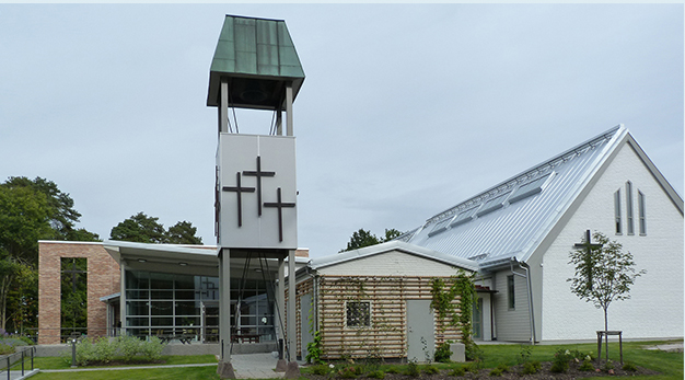 Entrén till Götalundens kyrka, glasad och med dekorativ tegelvägg och kors.