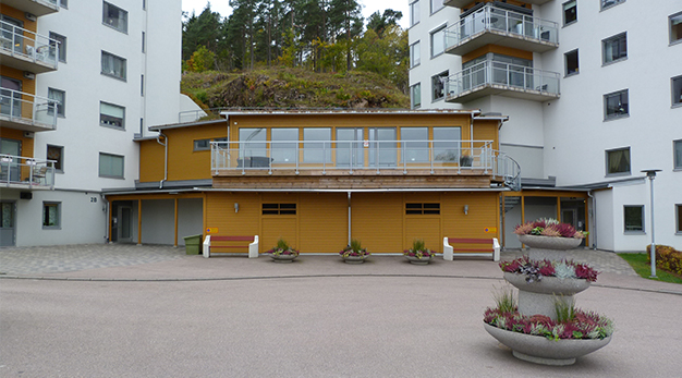 Bilden föreställer en byggnad mellan två höga hus. Byggnaden är gul. 