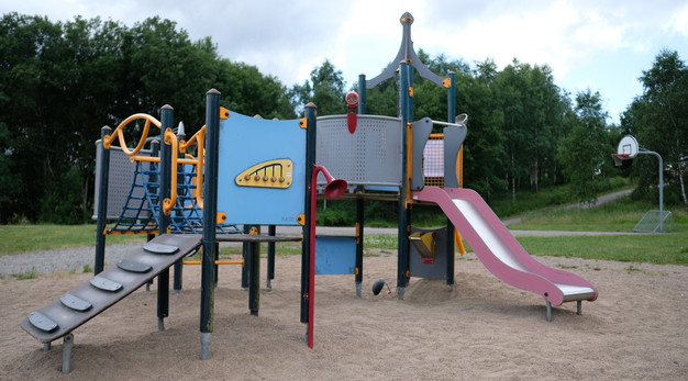 Bilden föreställer en lekställning med fyra små hus. Klätternät och broar binder husen samman. Huset till höger har en rutschkana. Huset till vänster har en stege. Huset är väldigt färgglatt. Det är rött, blått, gult, grått och grönt.  