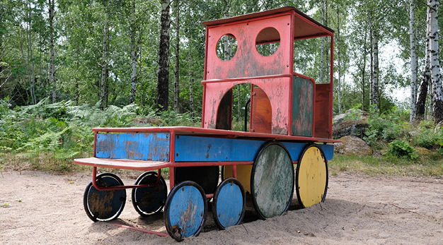 Bilden föreställer ett lekhus formad som ett tåglok. Loket är rött, blått och gult och är i trä. 