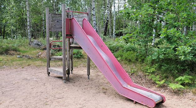 Bilden föreställer ett hus med en rutschkana. Kanan är röd och i bakgrunden syns flera träd och buskar.