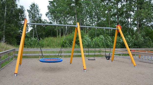 Fotografiet föreställer en gul gungställning med en kompisgunga, en vanlig gunga och en gunga för små barn. I bakgrunden syns flera buskar och träd. 