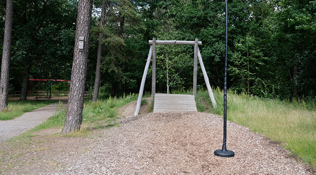 Bilden är ett fotografi över en linbana. I förgrunden syns sittdelen på linbanan och i bakgrunden avsatsen. Marken är täckt av träflis.