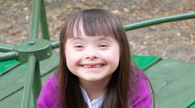 Mörkhårig flicka i lila kofta som ler stort mot kameran. 