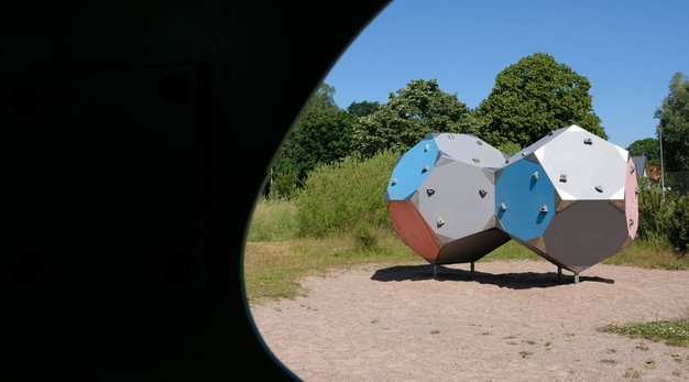 Bilden föreställer två stora klätterbollar som sitter en liten liten bit över marken. Bollarna är hexagon formade. De är röda, gråa och blåa. På bollarna sitter små handtag. 
