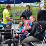Bilden föreställer vuxna och barn som fikar. De sitter på en uteservering. Vädret är mulet.  