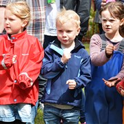 Bilden föreställer fyra barn i regnkläder med solen i ansiktet som sjunger och gestikulerar