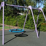 Bilden föreställer en ställning med en kompisgunga och en vanlig gunga. Ställningen är lila och gungan är svarta och blå. I bakgrunden syns en grön häck. 
