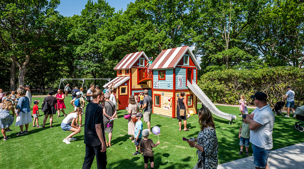 Bild på en färgglad lekbyggnad med två rutschkanor. Runt byggnaden syns många barn och vuxna.