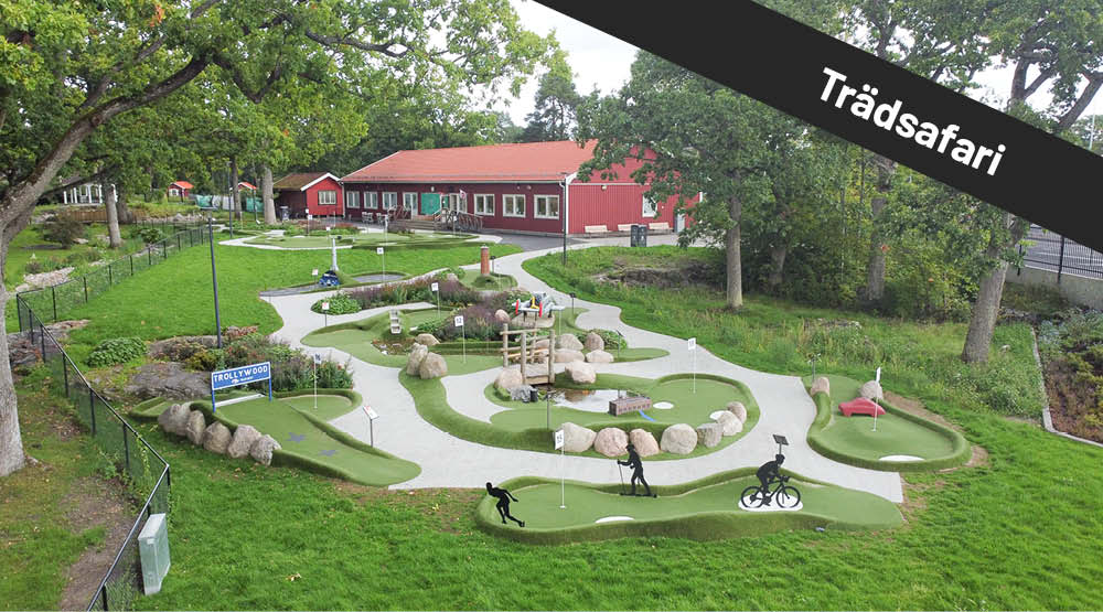 Äventyrsgolfbana med rött hus i bakgrunden. På bilden syns texten Trädsafari.