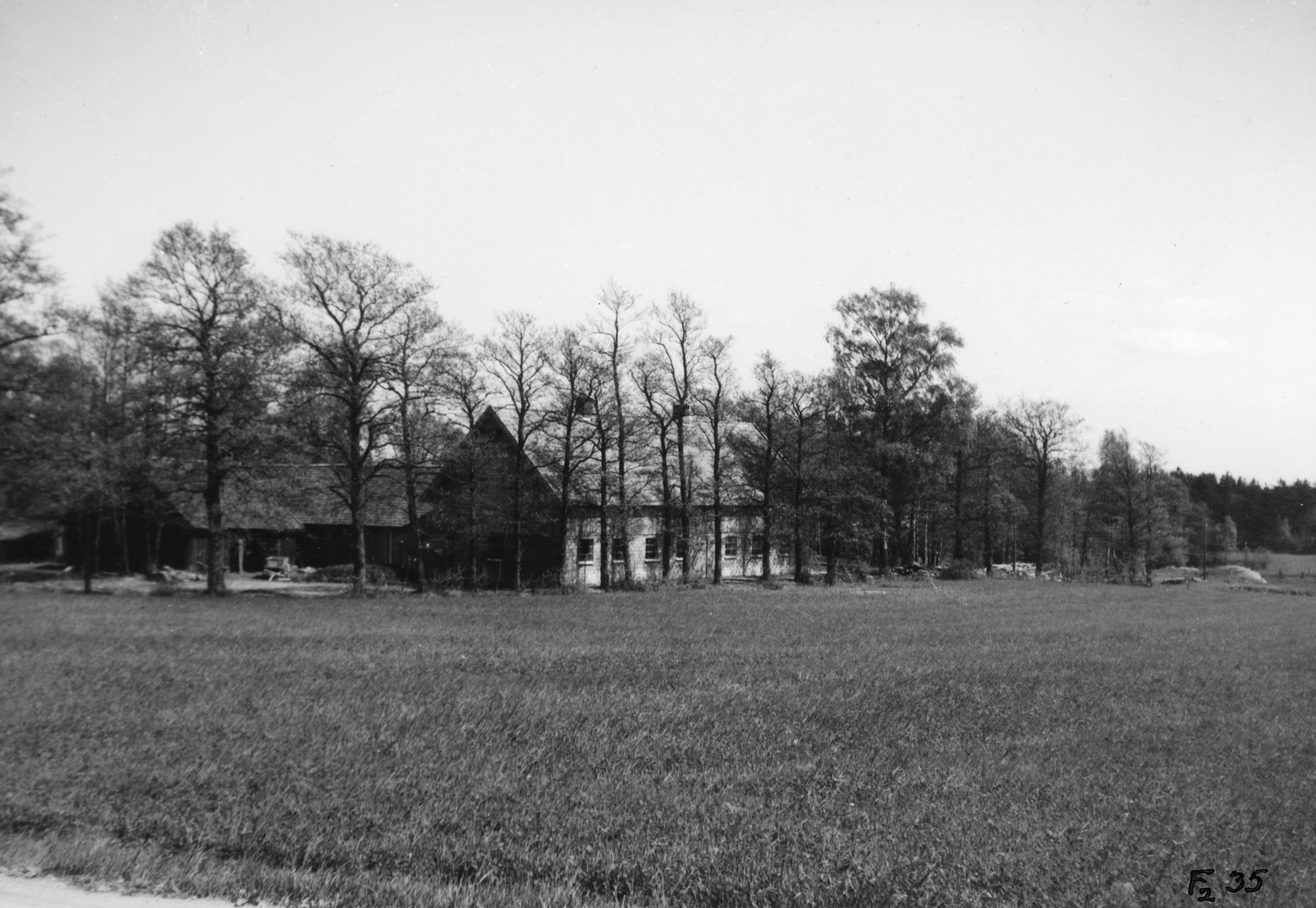 Svartvit bild på en ladugård. Ladugården är omringad av åker och träd.