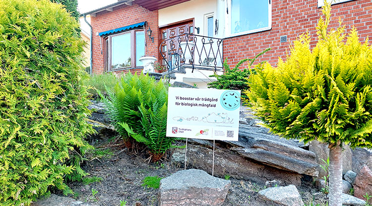 Bild på villaträdgård och en skylt med texten: ”Vi boostar vår trädgård för biologisk mångfald”