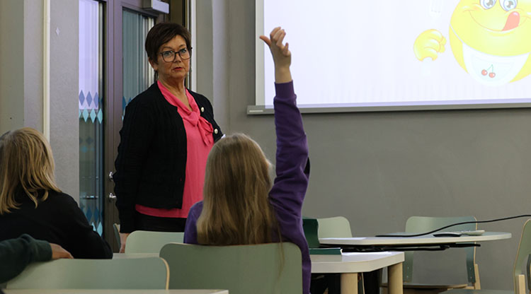 Elev räcker upp hand i klassrum. Lärare tittar på eleven.