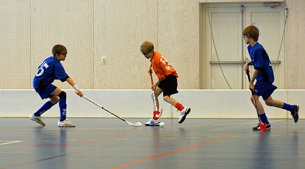 Barn som spelar innebandy inomhus.