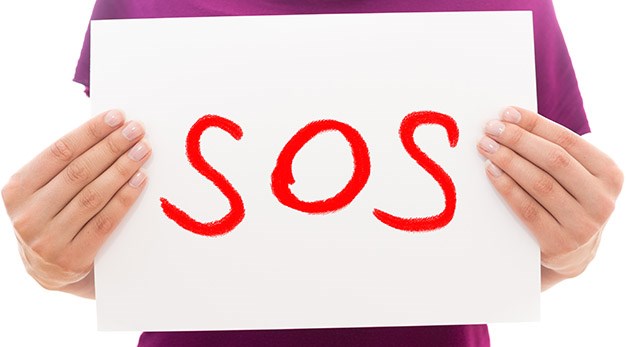 Två händer som håller upp en skylt med texten "SOS" i röda bokstäver