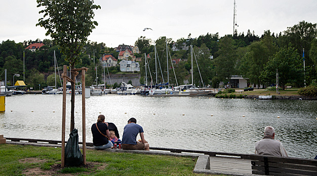 vybild över båthamnen. En familj sitter vid kajkanten och blickar ut över båthamnen på Spikön på andra sidan.