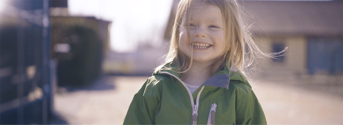 En glad flicka med grön jacka i utomhusmiljö. Foto.