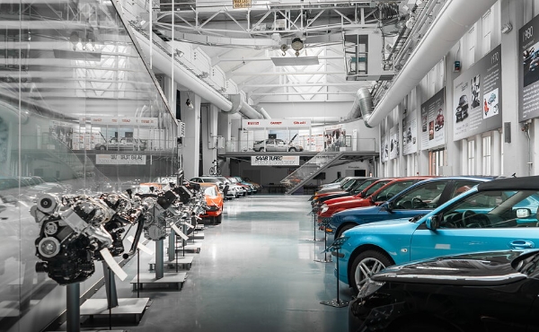 Saabs bilmuseum syns med flera olika bilmodeller i olika färger. Verkstadsliknande miljö. Foto.