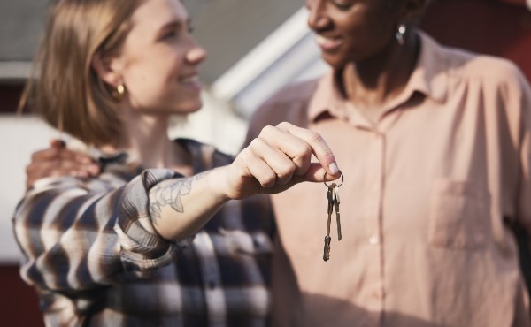 Kvinna vid entré till bostadshus klickar på touchskärm med postlådor bakom ryggen. Foto.