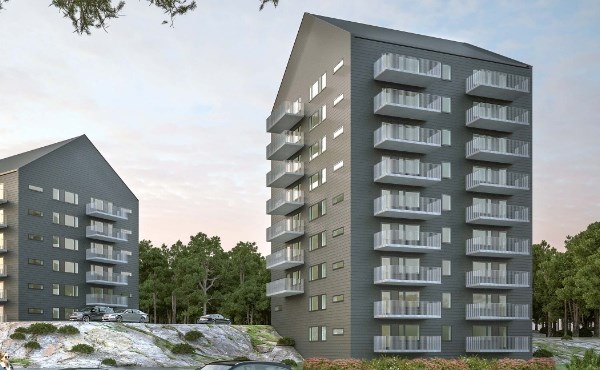 Två gråa nybyggda bostadshus på 15-våningar vid ett skogsbryn. Foto.