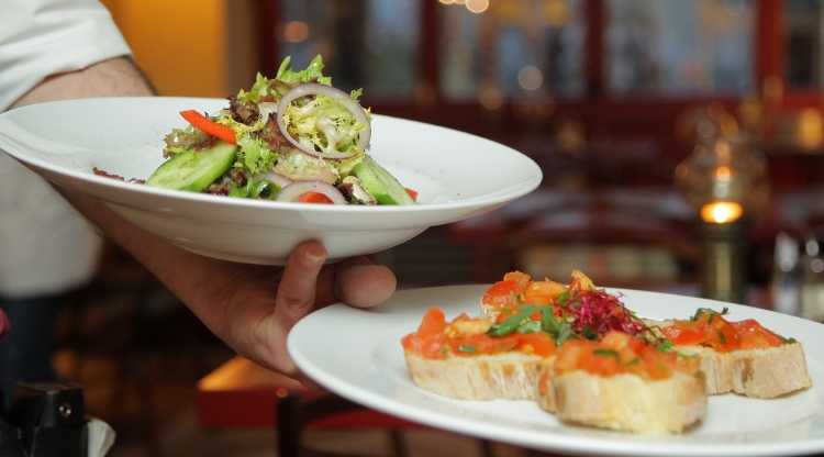 Två tallrikar med lyxigt upplagd mat hålls fram av en hand. Foto.