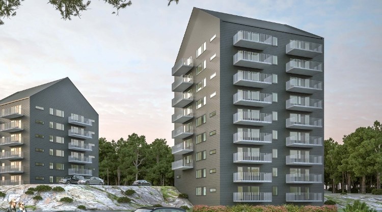 Två gråa nybyggda bostadshus på 15-våningar vid ett skogsbryn. Foto.