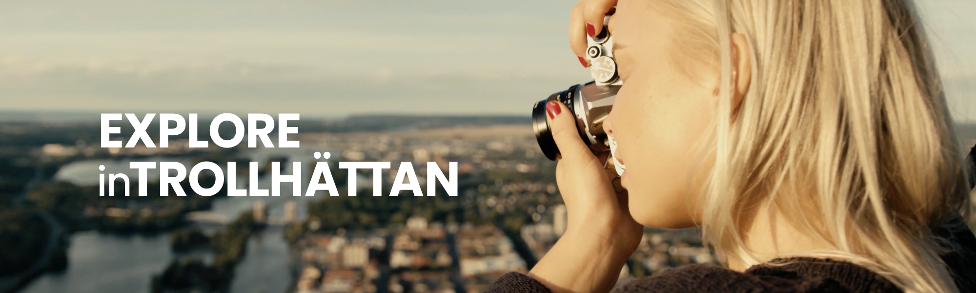 Kvinna med kamera fotar staden från hög utsiktsplats. Bildtext säger Explore inTrollhättan. Foto.