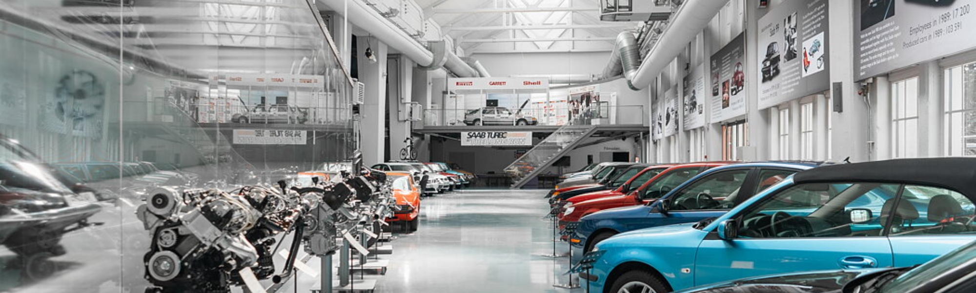 Saabs bilmuseum syns med flera olika bilmodeller i olika färger. Verkstadsliknande miljö. Foto.