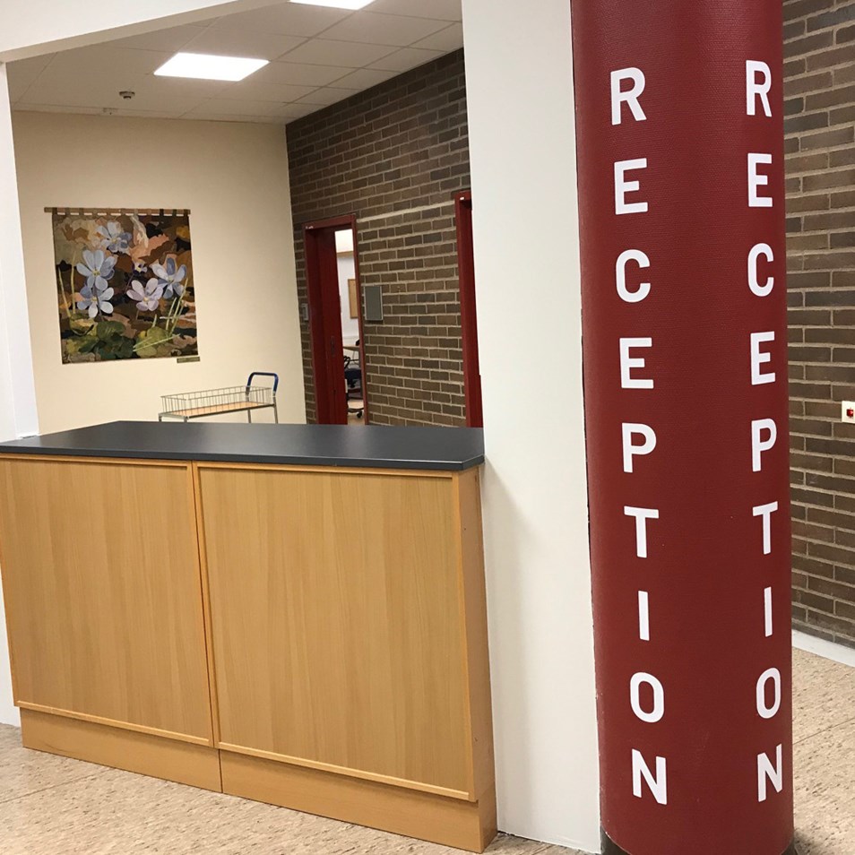 Bilden föreställer den tillfälliga receptionen under uppbyggnad. Till höger i bild står en stor röd pelare med texten reception. Till vänster om pelaren är en disk i brunt trä med svart bänkskiva. Bakom receptionsdisken, till vänster, syns en stor tavla med blommor på och till höger är det en brun tegelvägg. 