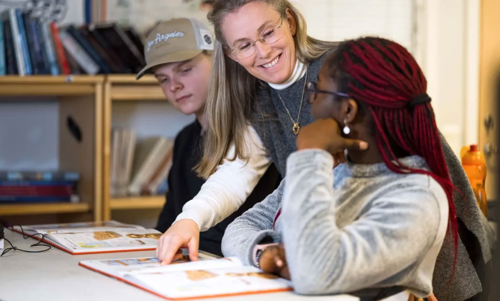 En pedagog pekar i en bok och förklarar en uppgift för en elev. Foto.