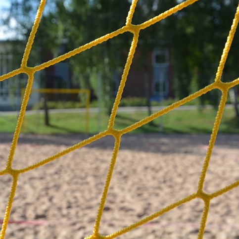 Bilden är en närbild över ett nät till ett fotbollsmål. Nätet är gult och i bakgrunden syns sand.  