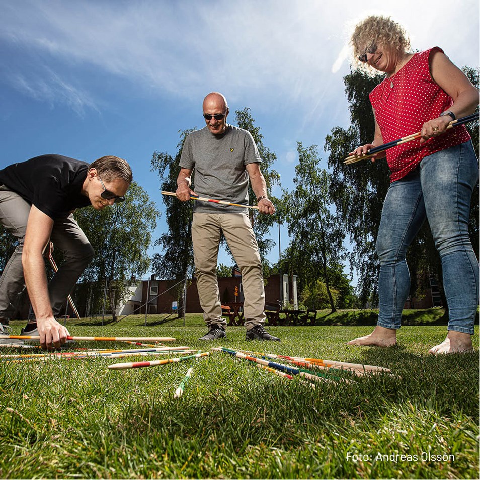 Två kvinnor och en man som spelar plockepinn på gräset