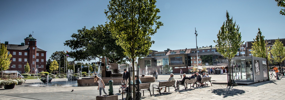 Drottningtorget i Trollhättan en solig och varm dag. Människor i alla åldrar vistas på torget.