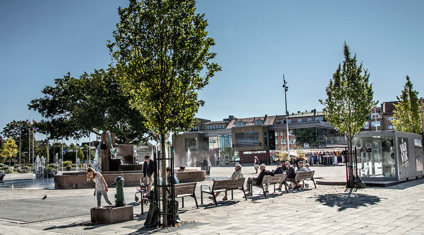 Drottningtorget Trollhättan, människor sitter på parkbänkar. 