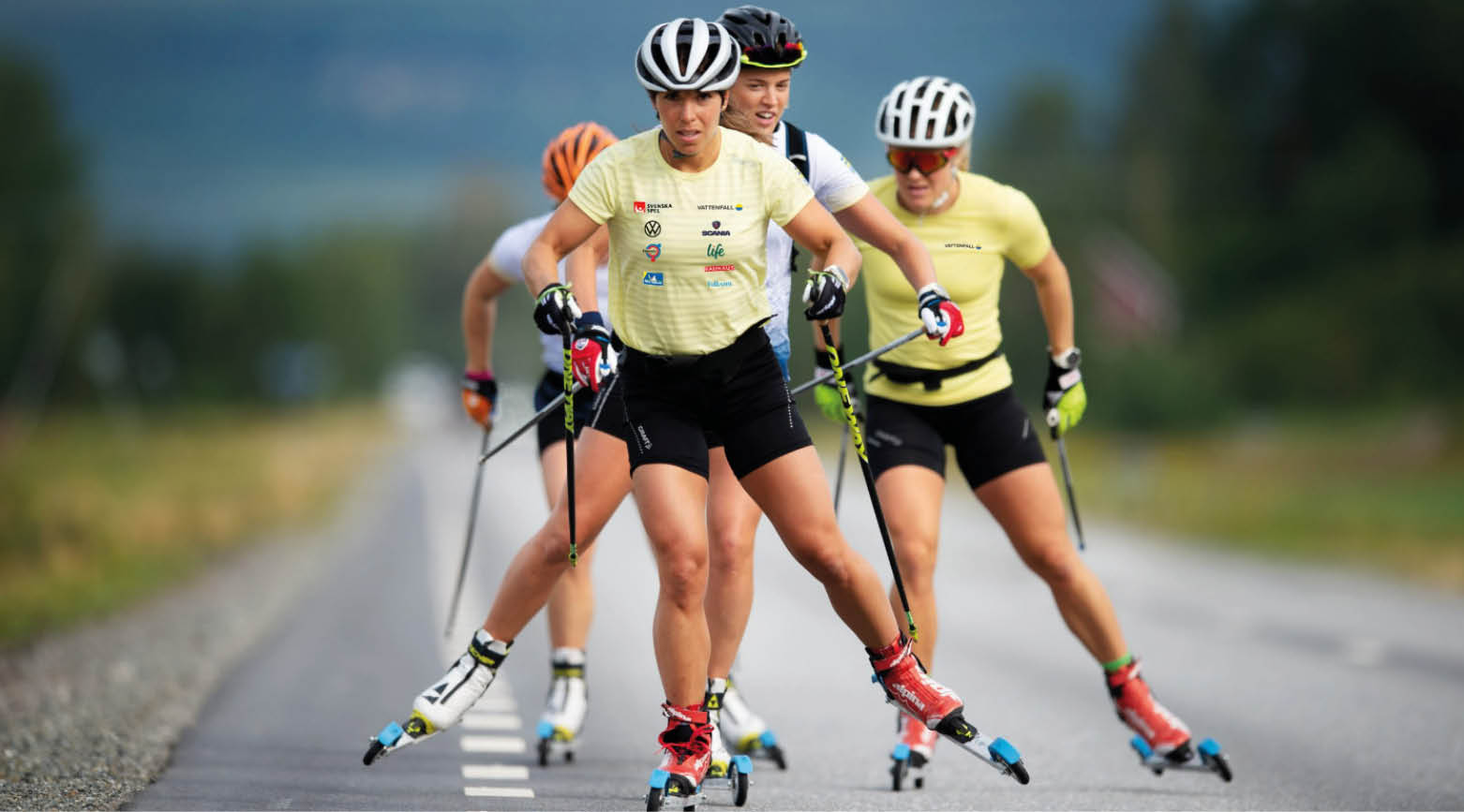 En bild på tjejerna i svenska skidlandslaget på rullskidor med Charlotte Kalla längst fram