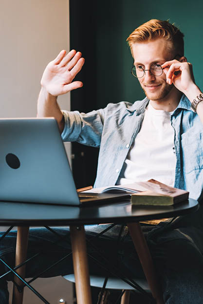 Man som vinkar i digitalt möte vid laptop
