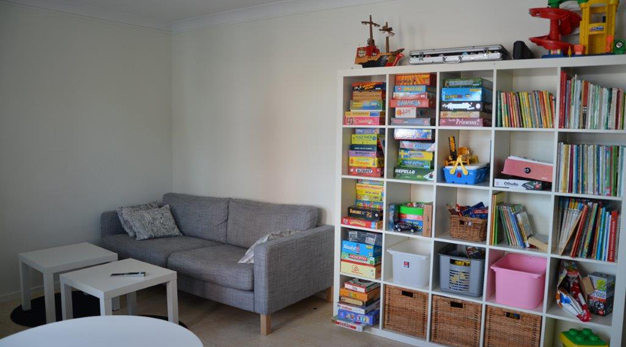 En soffa står bredvid en bokhylla fylld med leksaker och böcker.