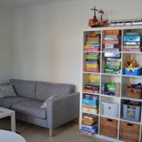 En soffa står bredvid en bokhylla fylld med leksaker och böcker.