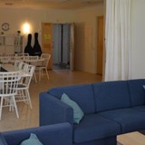 En stor soffa. Bakom soffan står två matsalsbord med flera stolar runt omkring borden.