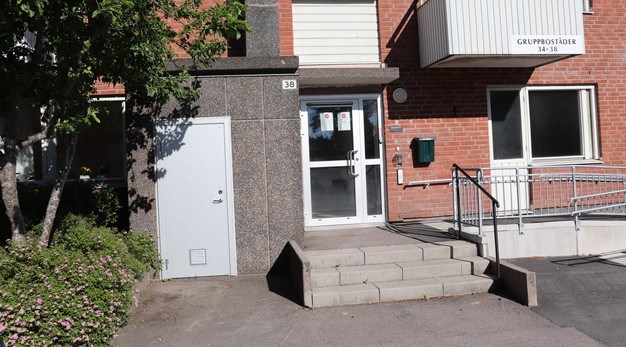 Ingång och ytterdörr till Humlevägen 38. På ena sidan syns en handikappanpassad ingång och på andra sidan av ingången en buske.