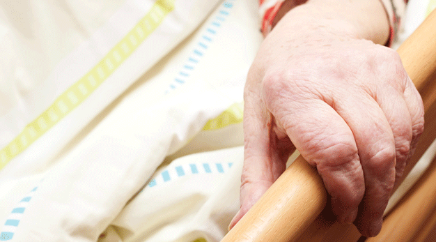 Bild på en äldre persons hand som håller om kanten på en säng. 