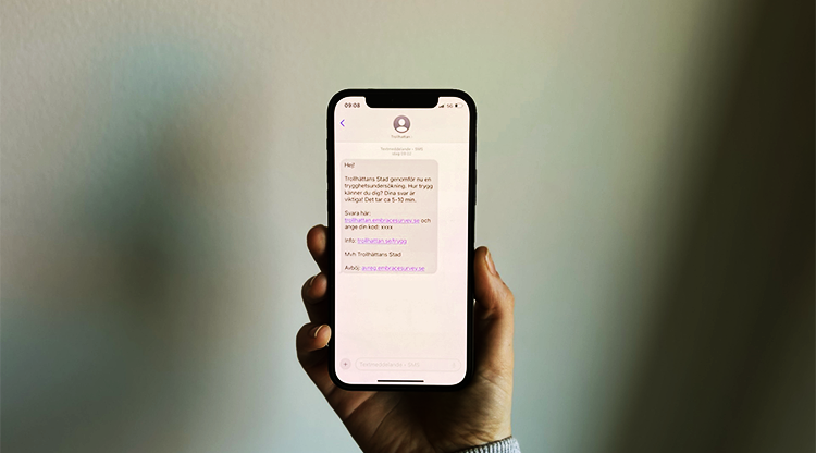 "En hand håller en mobiltelefon. På skärmen: Hej! Trollhättans Stad genomför nu en trygghetsundersökning. Hur trygg känner du dig? Dina svar är viktiga! Det tar ca 5-10 minuter. Svara här: trollhattan.embracersurvey.se och ange din kod. Info: trollhattan.se/trygg Med vänliga hälsningar, Trollhättans stad."