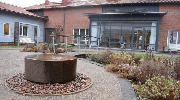 En stor sten med ett vattenspel står utplacerat i en trädgård. I bakgrunden syns en inglasad balkong på Nordängen. 