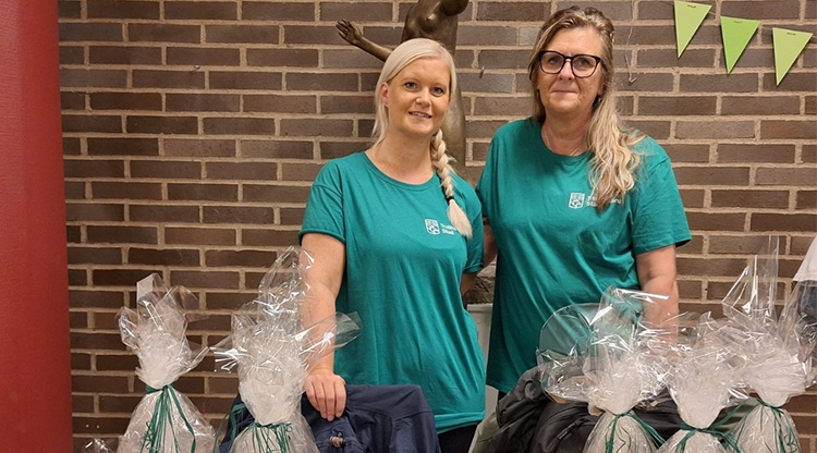 Två personal i grön t-shirt står bakom ett mässbord där de säljer ljus, vetekuddar och annat