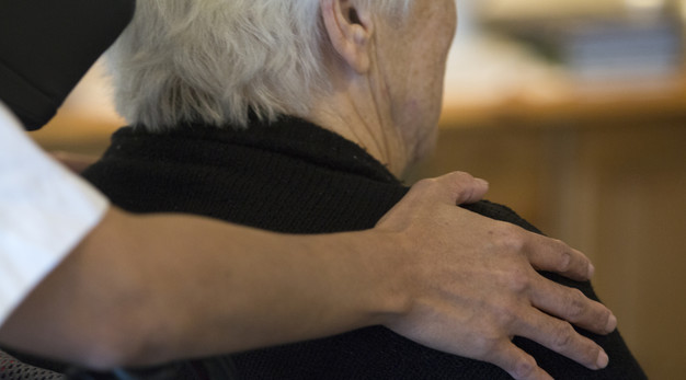 Vårdpersonal håller handen på axeln på en äldre person på ett boende.