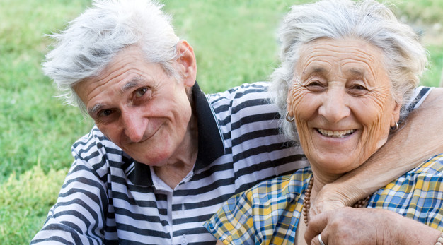 Ett äldre par sitter på en gräsmatta utomhus och håller om varandra.