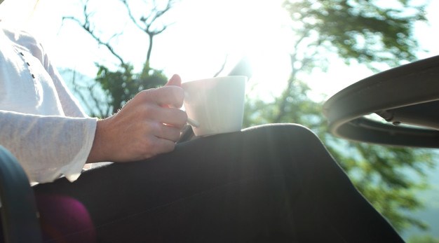 Person sitter utomhus och tar en kaffe i solen.
