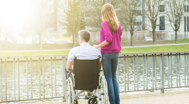 Kvinna står bredvid en man i rullstol och tittar ut över en kanal.