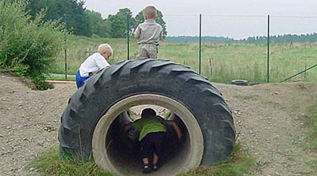 Tre barn som leker med ett traktordäck
